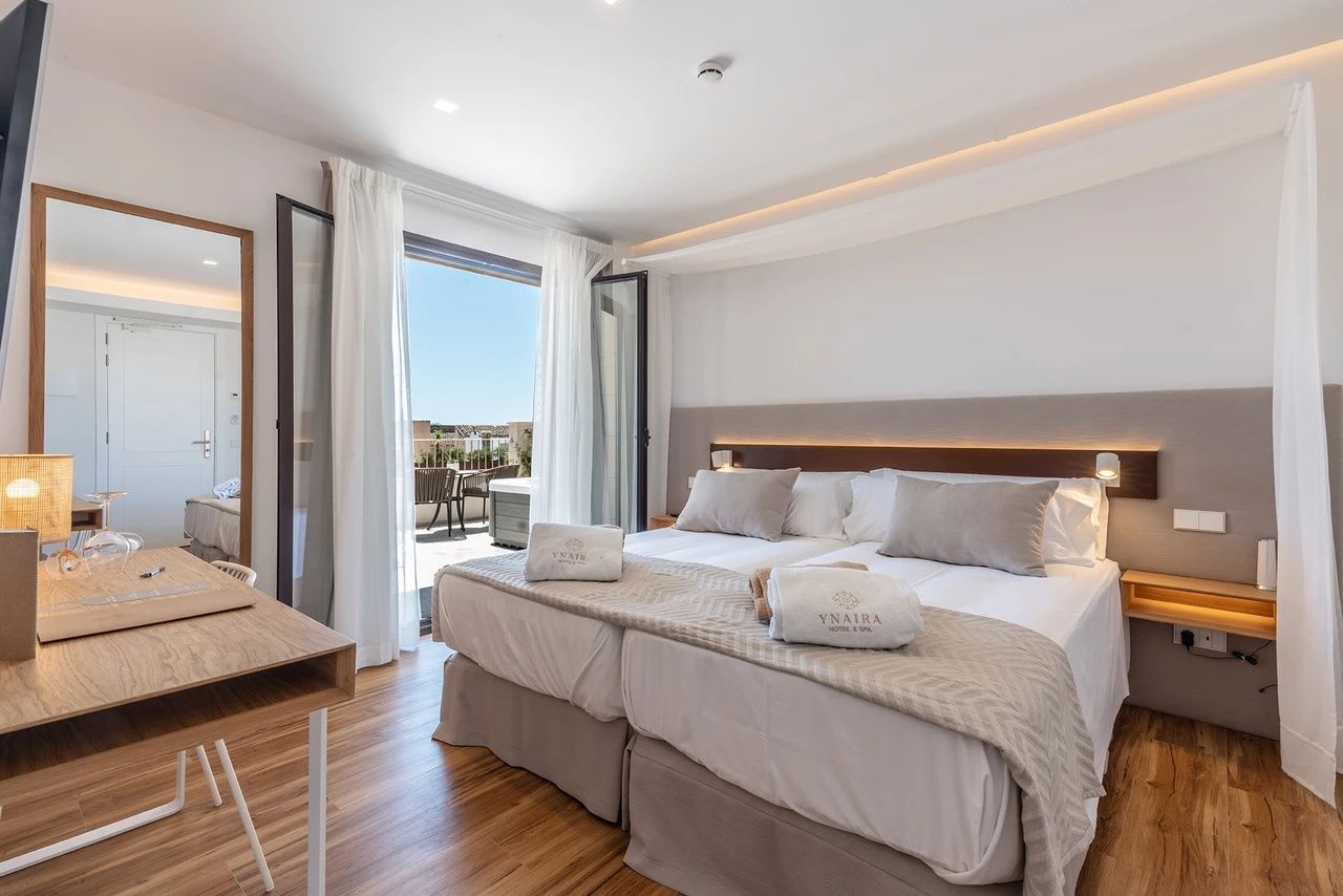 Geräumiges Schlafzimmer mit aufgeteiltem Doppelbett und offener Balkontür zur Terrasse.