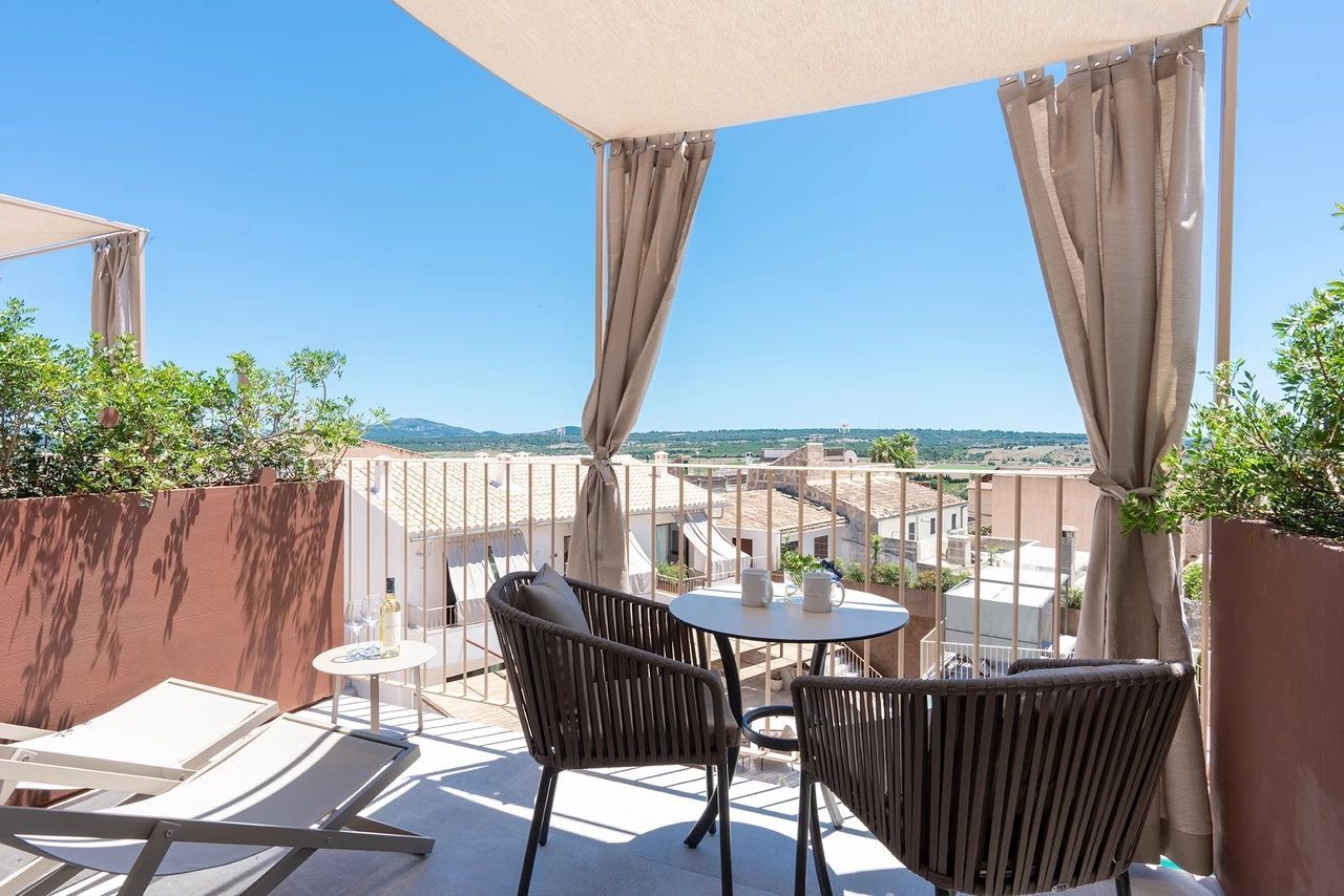 Möblierte Terrasse unter einem Sonnensegel mit Blick über Hausdächer und die grüne Landschaft.