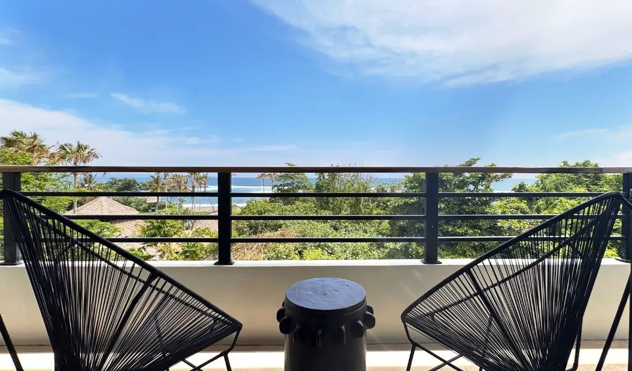 Balkon mit zwei Stühlen und Aussicht auf grüne Palmen sowie das blaue Meer.