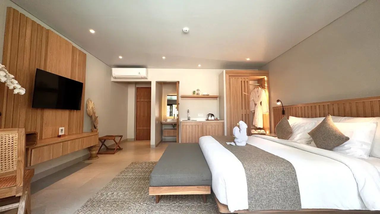 Blick durch das Hotelzimmer auf den Holzschrank, die Minibar und den Badbereich.