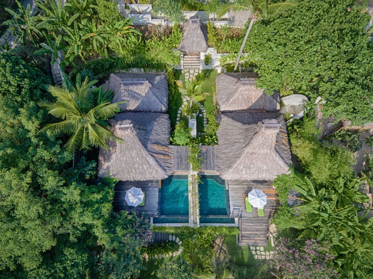 Villa mit Schilfdach und privatem Pool zwischen Palmen im NIHI Sumba, von oben fotografiert