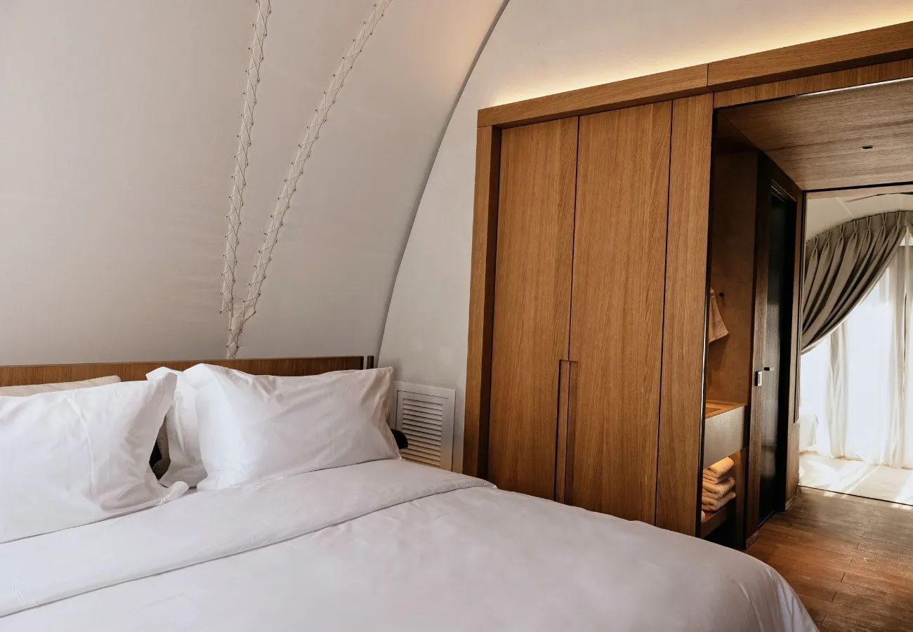 Doppelbett mit weißer Bettwäsche neben einem Holzschrank unter einer gewölbten Zeltdecke.