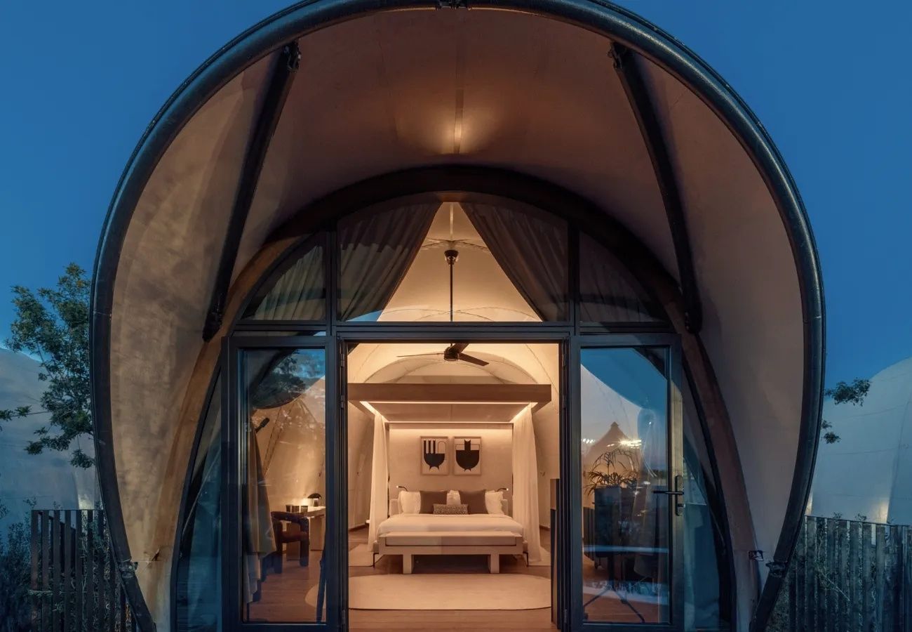 Beleuchtete Zelt-Lodge am Abend mit Blick durch die Glasfront ins Zimmer.