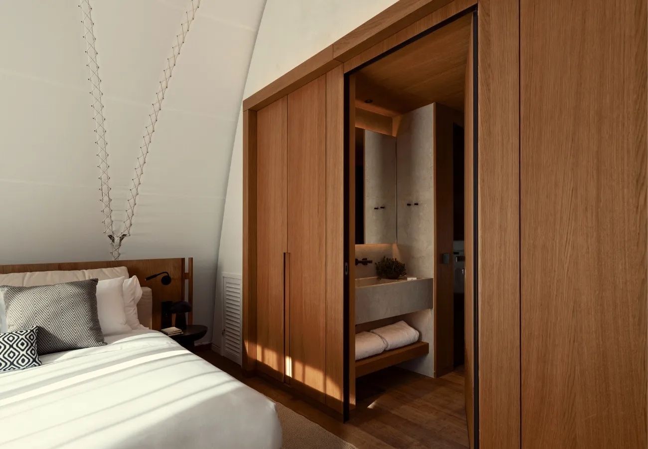 Ein Holzschrank mit Schiebetür gibt den Blick frei auf ein angrenzendes Badezimmer.