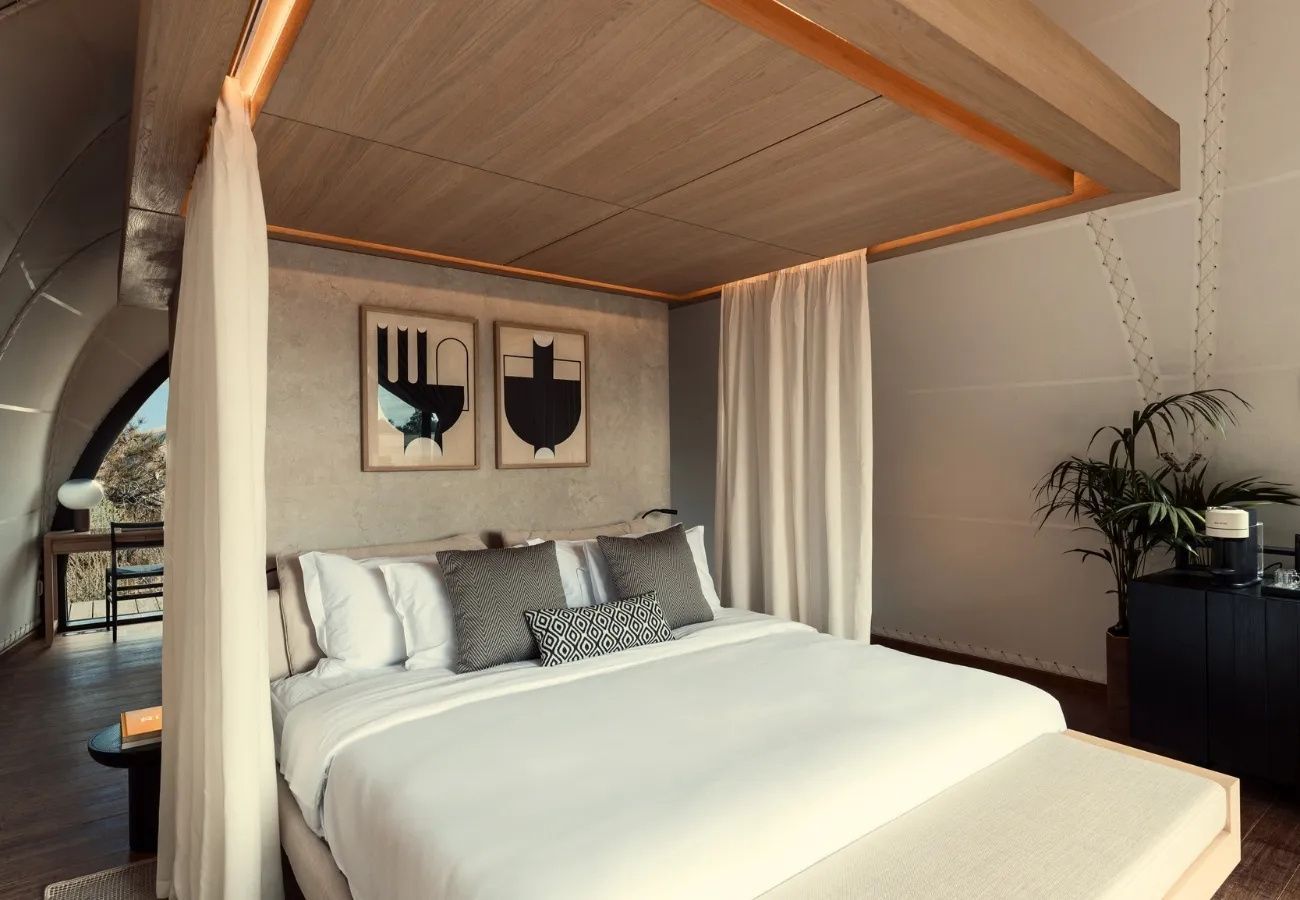 Doppelbett mit hellen Kissen, Vorhängen und Holzdecke in einer modernen Hotelunterkunft.