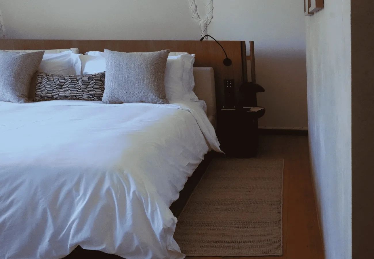 Doppelbett mit weißer Bettwäsche, Kissen und Teppich im Hotelzimmer.