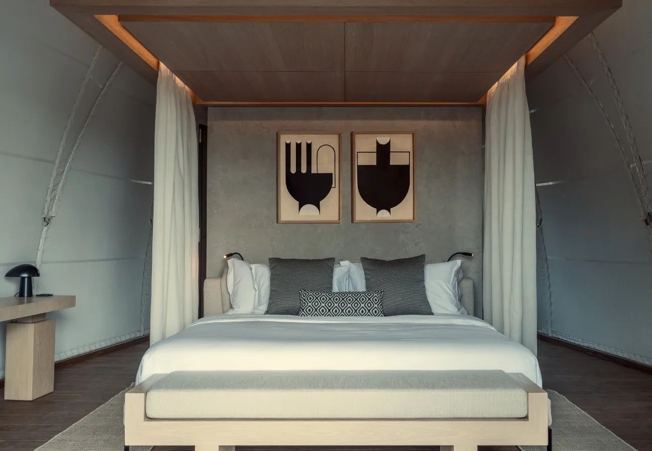 Doppelbett mit Holzbaldachin, grauen Kissen und Kunstwerken an der Wand.