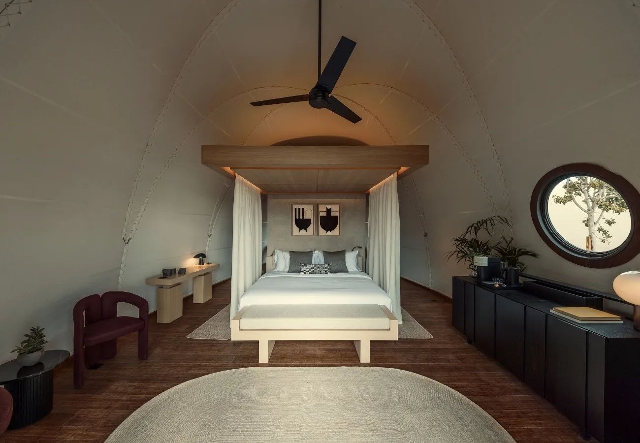 Großes Zeltzimmer mit zentralem Doppelbett, runder Teppich, Deckenventilator und dunklen Möbeln.
