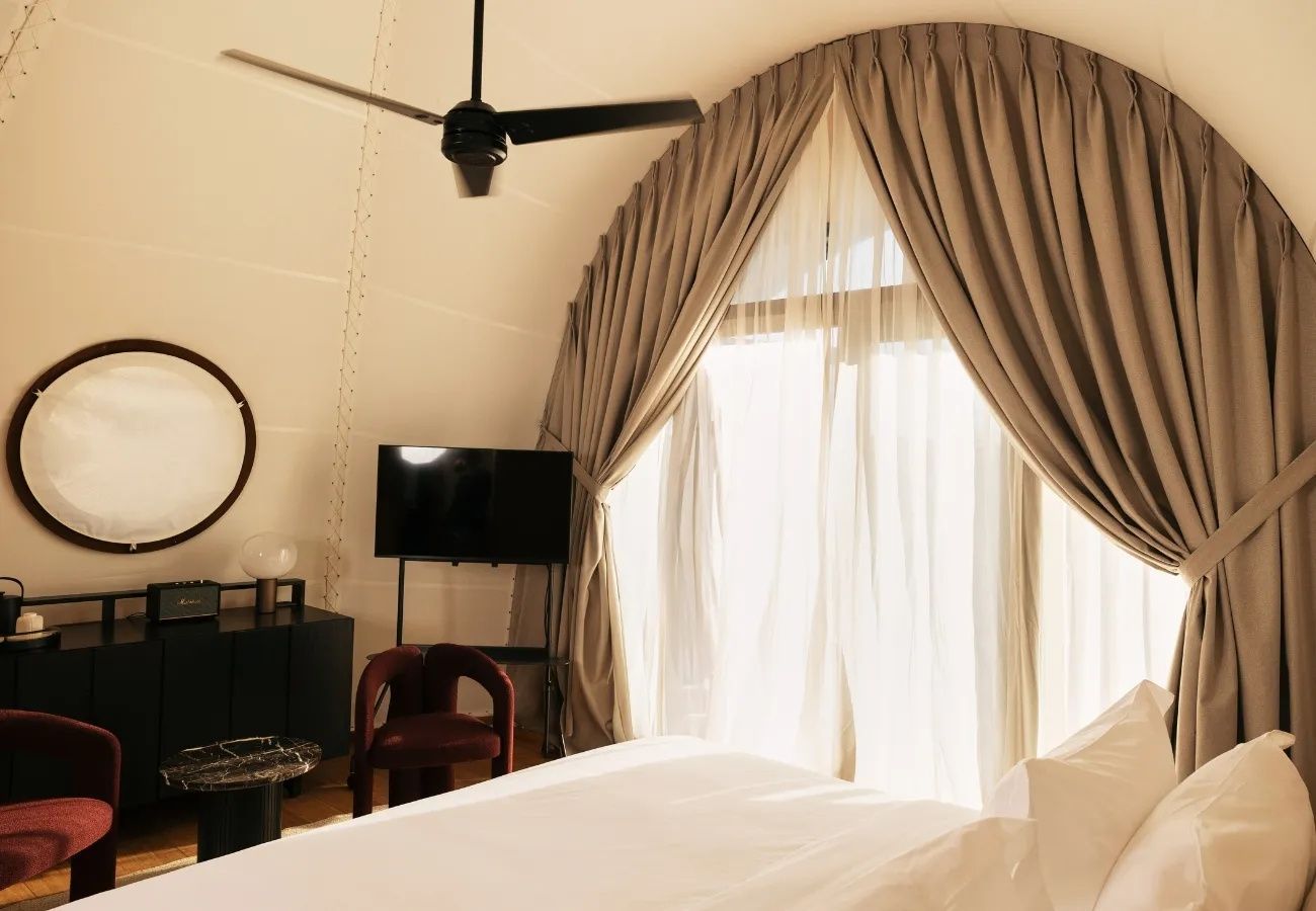 Schlafbereich mit Fernseher, Deckenventilator und Vorhängen an einer großen Fensterfront.