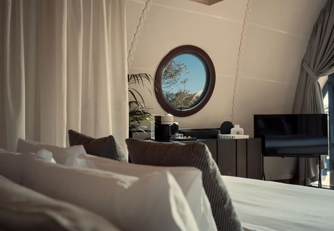 Blick über ein Bett auf ein rundes Fenster mit Aussicht ins Freie.