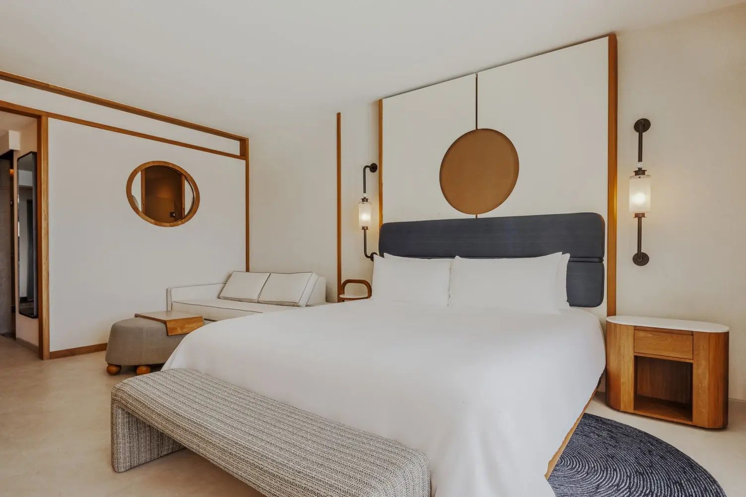 Helles Hotelzimmer mit großem Doppelbett, weißer Bettwäsche und gemütlicher Sitzecke.