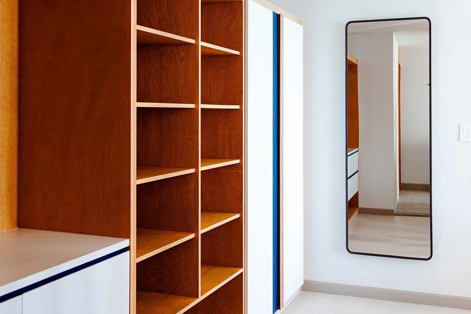 Ein offenes Holzregal im Ankleidebereich eines Hotelzimmers neben einem schmalen Wandspiegel.