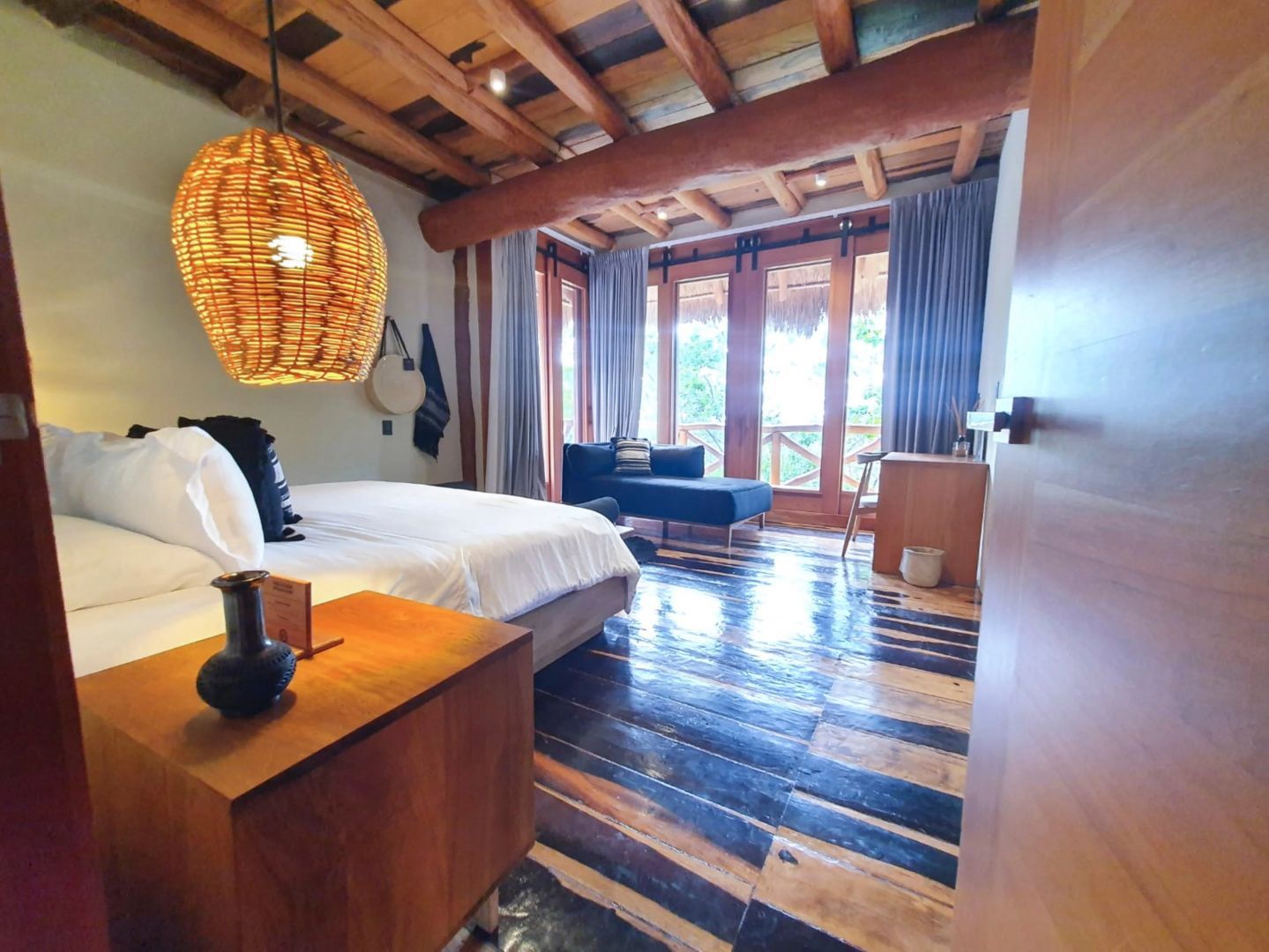 Hotelzimmer mit Holzdecke, großem Bett, einer geflochtenen Lampe und dunklem Holzboden.