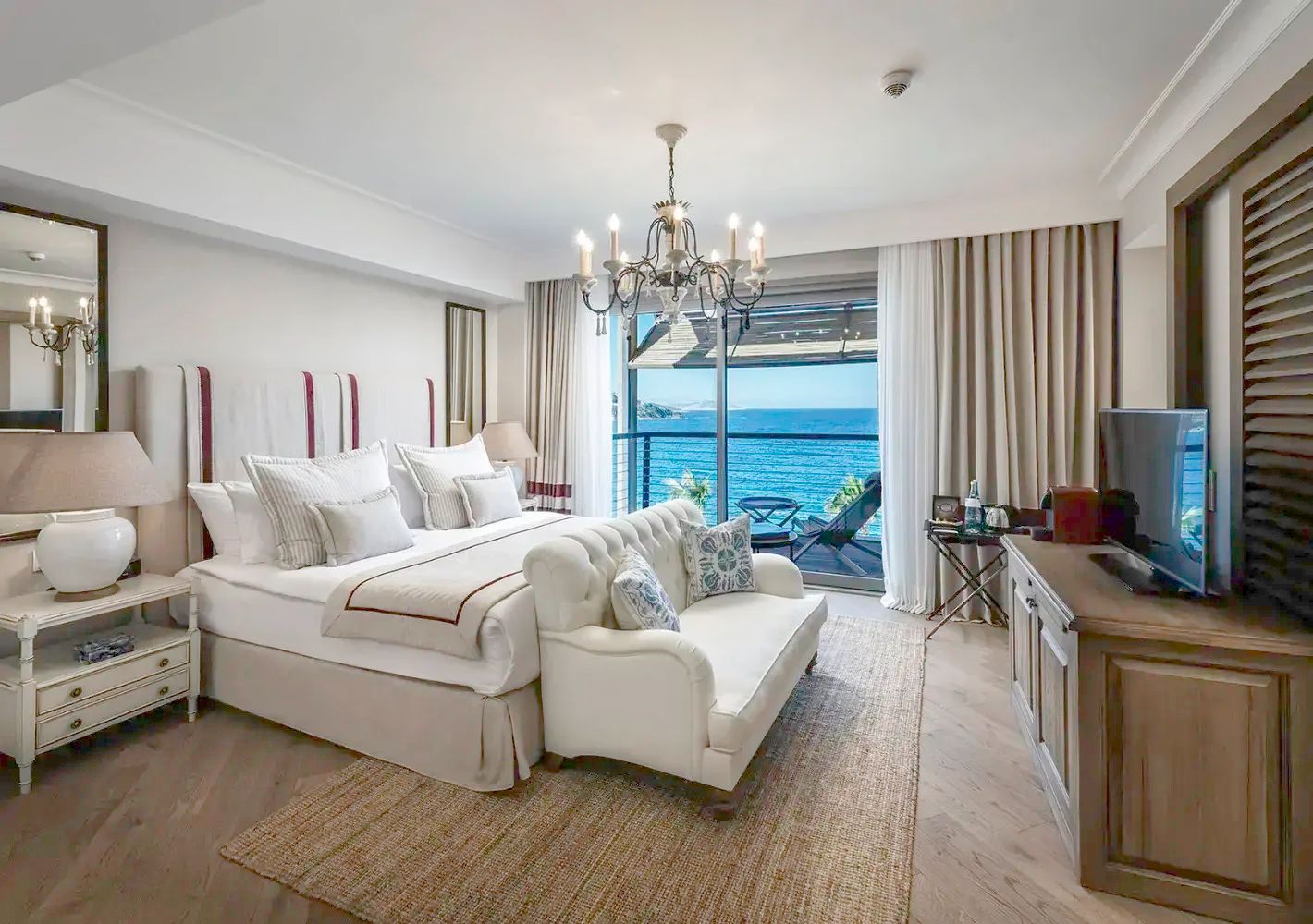 Helles Hotelzimmer mit Doppelbett, Polsterbank und Balkon mit freiem Blick auf das Meer.