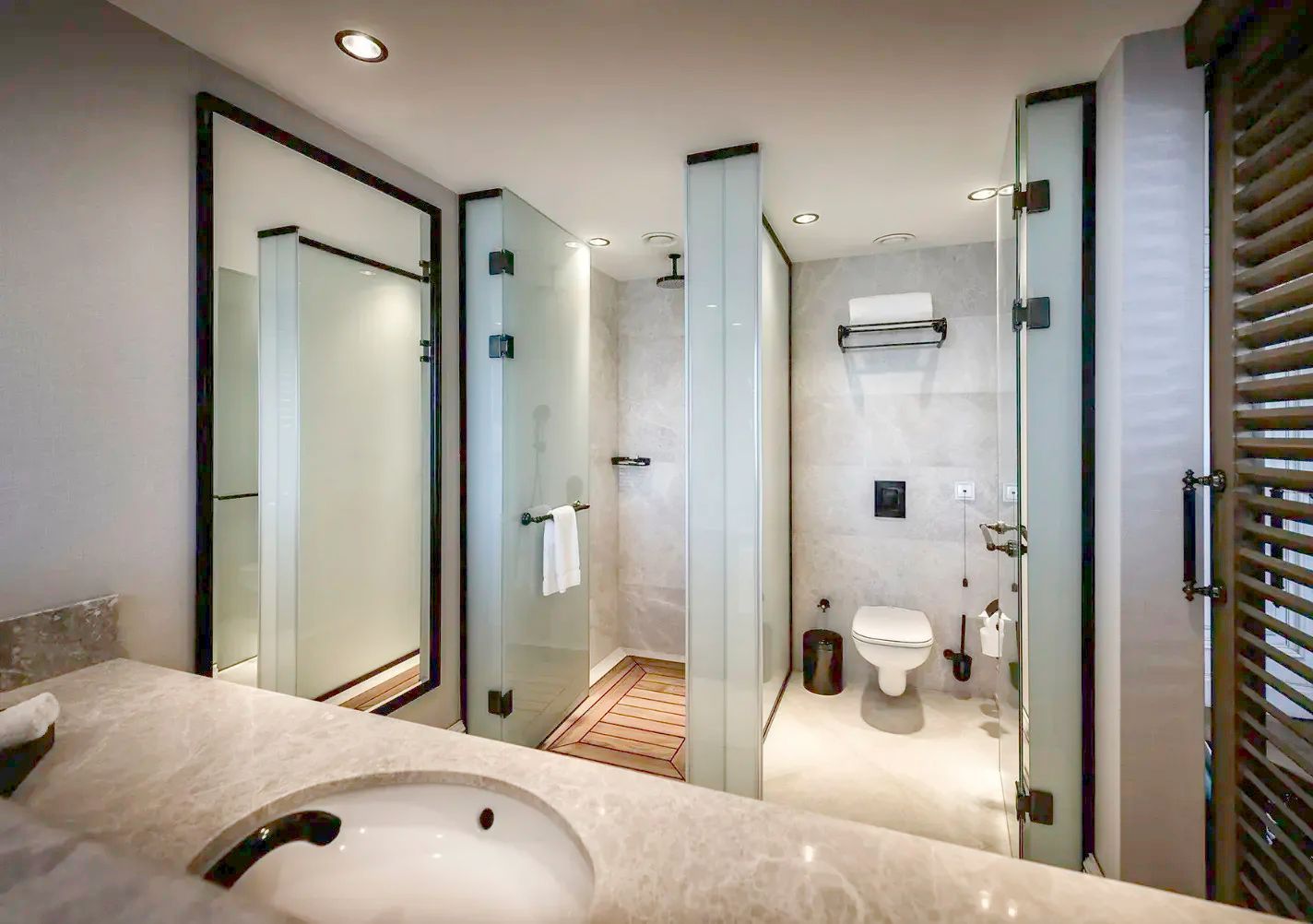 Modernes Badezimmer mit Glasabtrennungen für Dusche und WC sowie einem Waschtisch im Vordergrund.