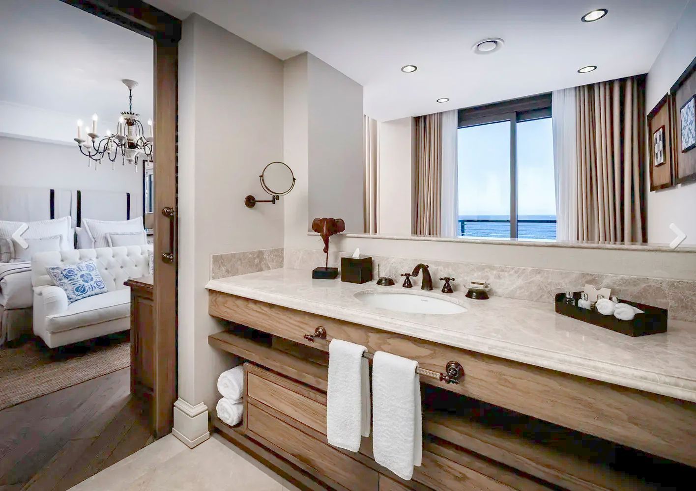Badezimmer mit hölzernem Waschtisch, großem Spiegel und Durchgang zum Schlafzimmer.