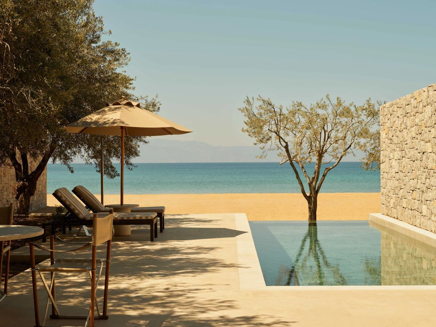 Zwei Sonnenliegen und ein Schirm am Pool mit Blick auf Strand und Meer.