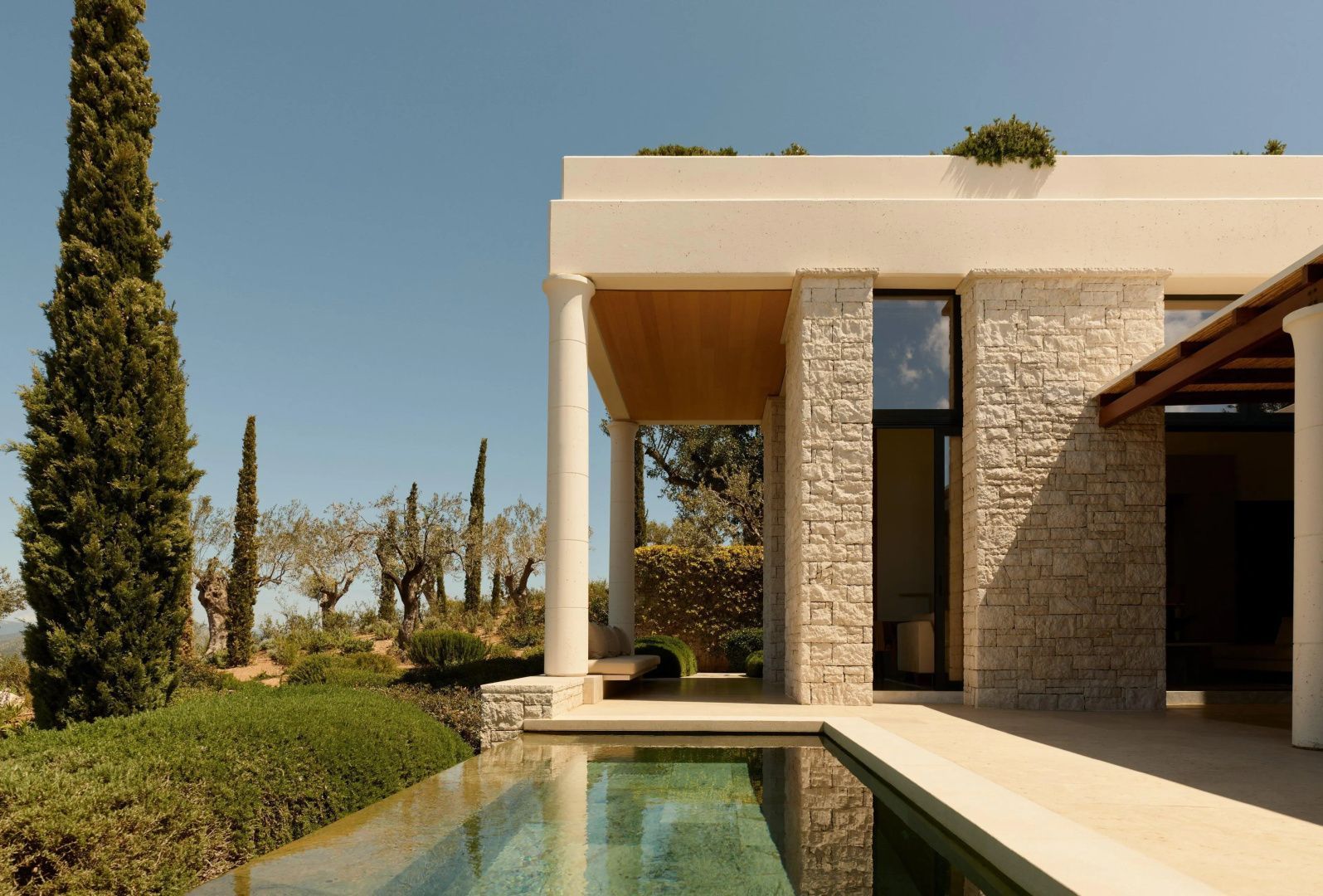 Moderne Hotelvilla aus hellem Naturstein mit Säule, Terrasse und umgebendem Garten.