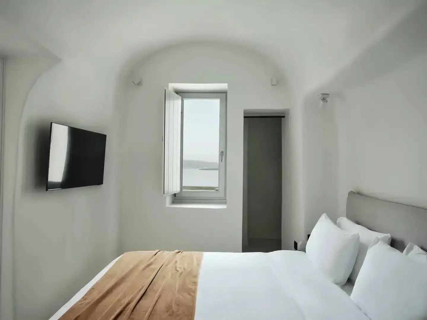 Weißes Schlafzimmer mit Gewölbedecke, Doppelbett und Fenster mit Meeresblick.