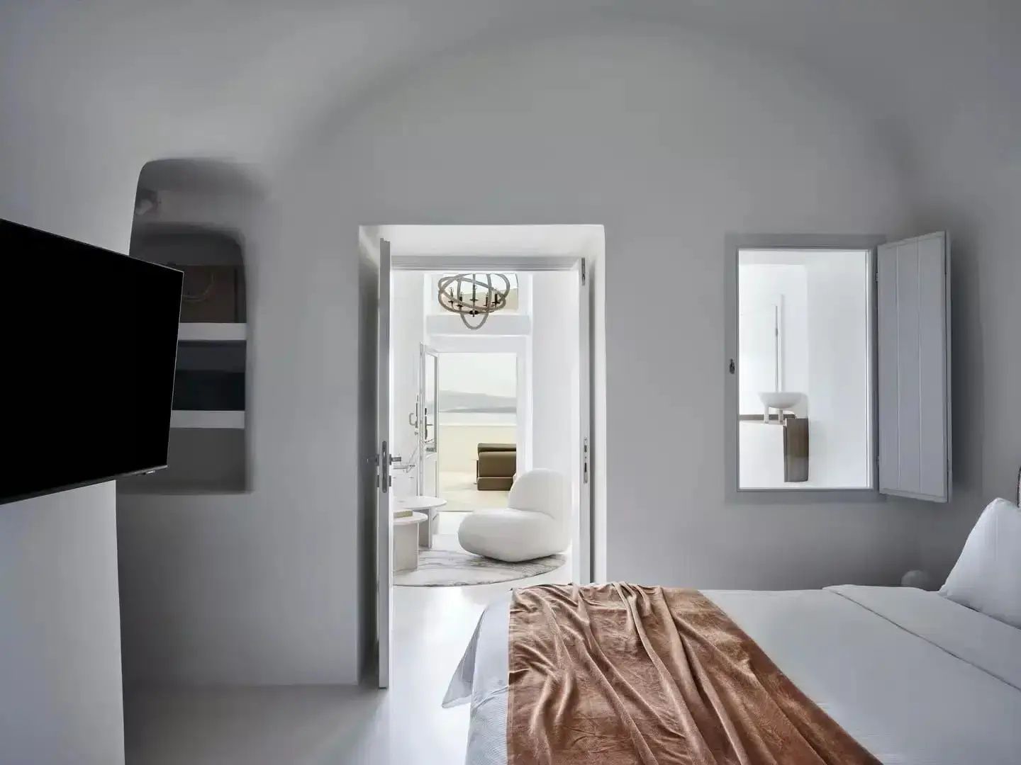 Blick vom Schlafzimmer durch offene Türen in einen Wohnbereich mit weißem Sessel.
