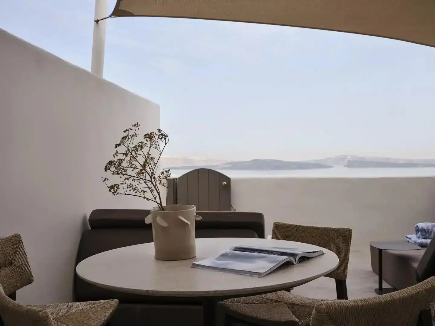 Terrasse mit Esstisch, Stühlen und Ausblick auf das Meer unter einem Sonnensegel.