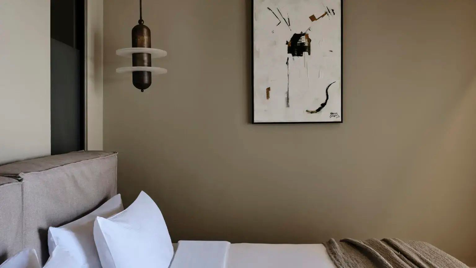 Weißes Kissen auf einem Bett neben einer modernen Hängeleuchte und einem Gemälde.