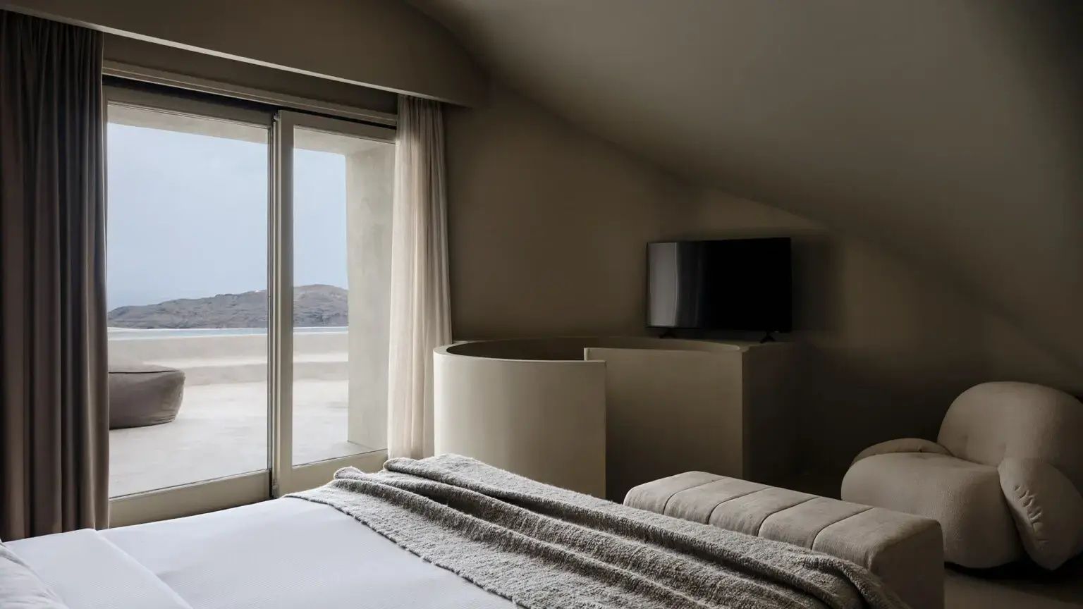 Blick aus dem Schlafzimmer mit Doppelbett und Fernseher auf die Terrasse und das Meer im Hintergrund.