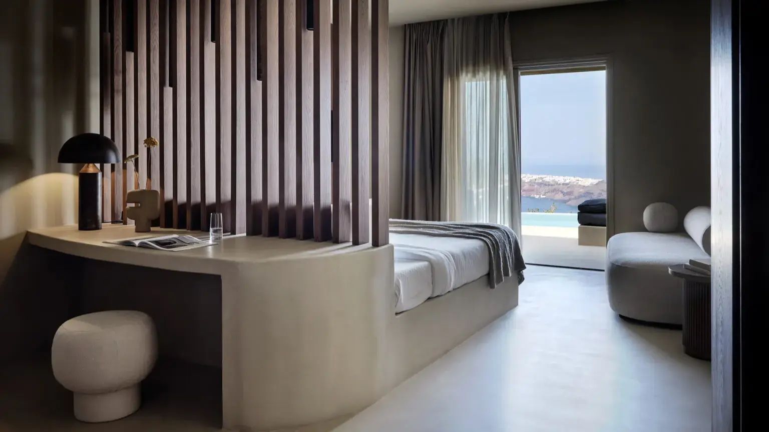 Hell gestaltete Suite mit Holzlatten-Trennwand, Bett und Ausblick auf den Pool und das Meer.