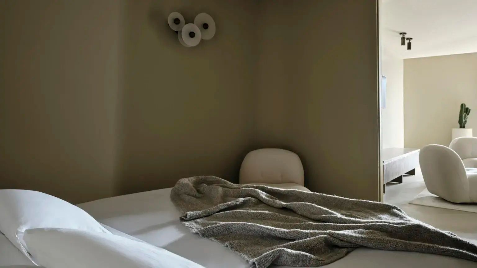 Ecke eines Schlafzimmers mit gemachtem Bett, Decke und runder Wandleuchte.
