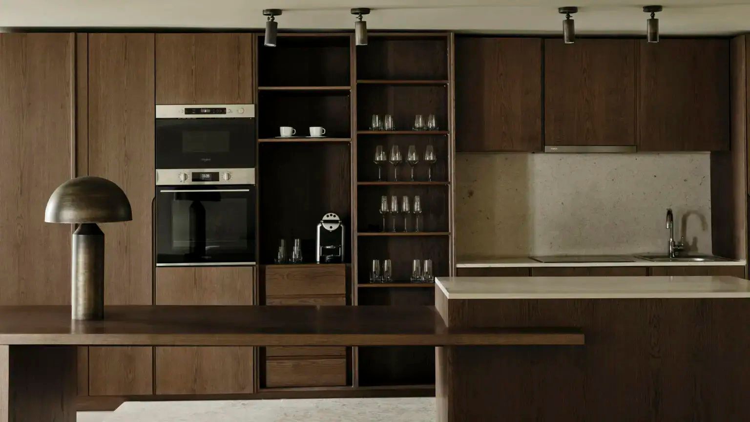 Küchenzeile aus dunklem Holz mit Einbaugeräten, Kaffeemaschine und Gläsern.