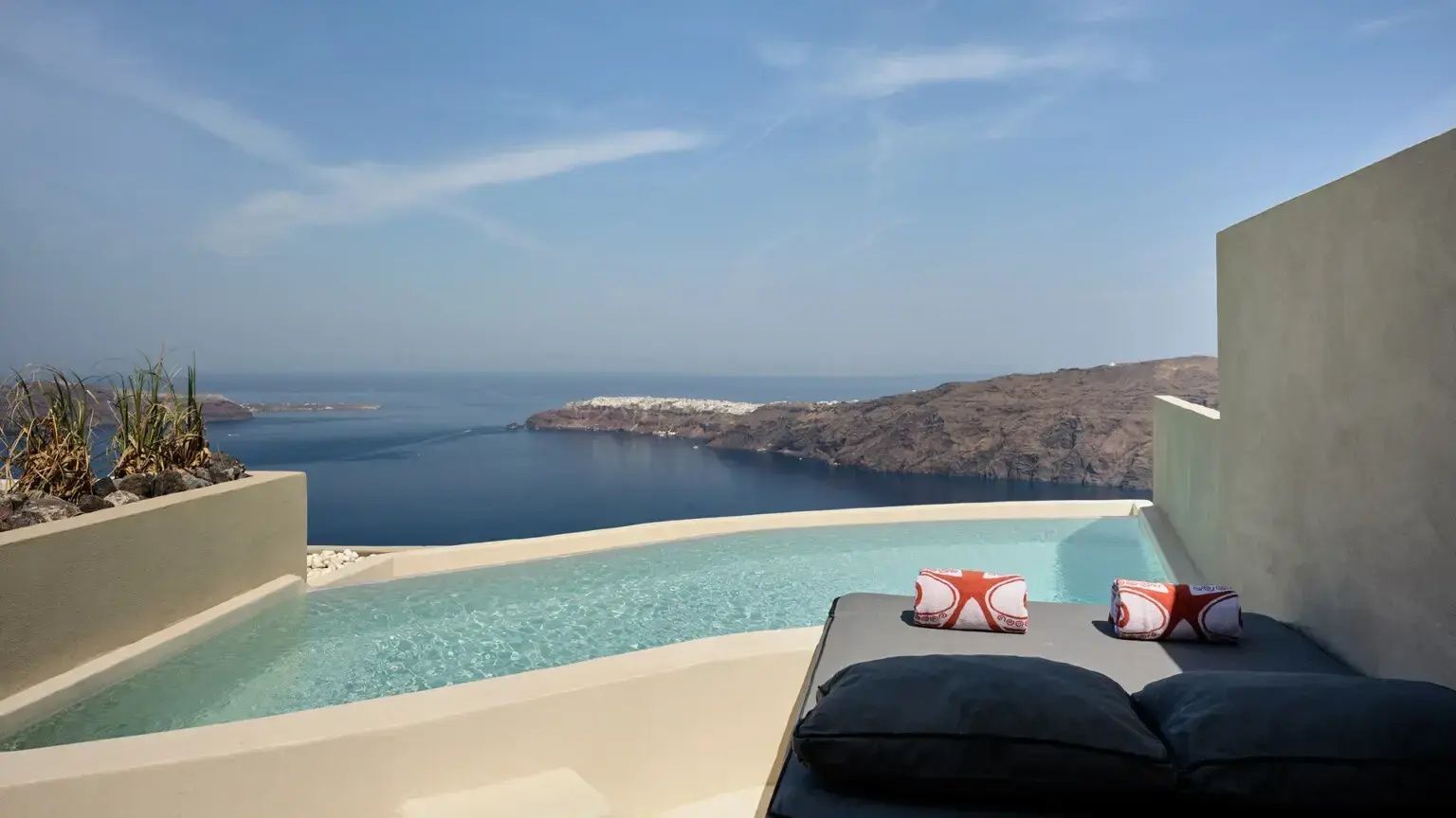 Infinitypool mit einer Liege im Vordergrund und Ausblick auf das Meer sowie Felsen.