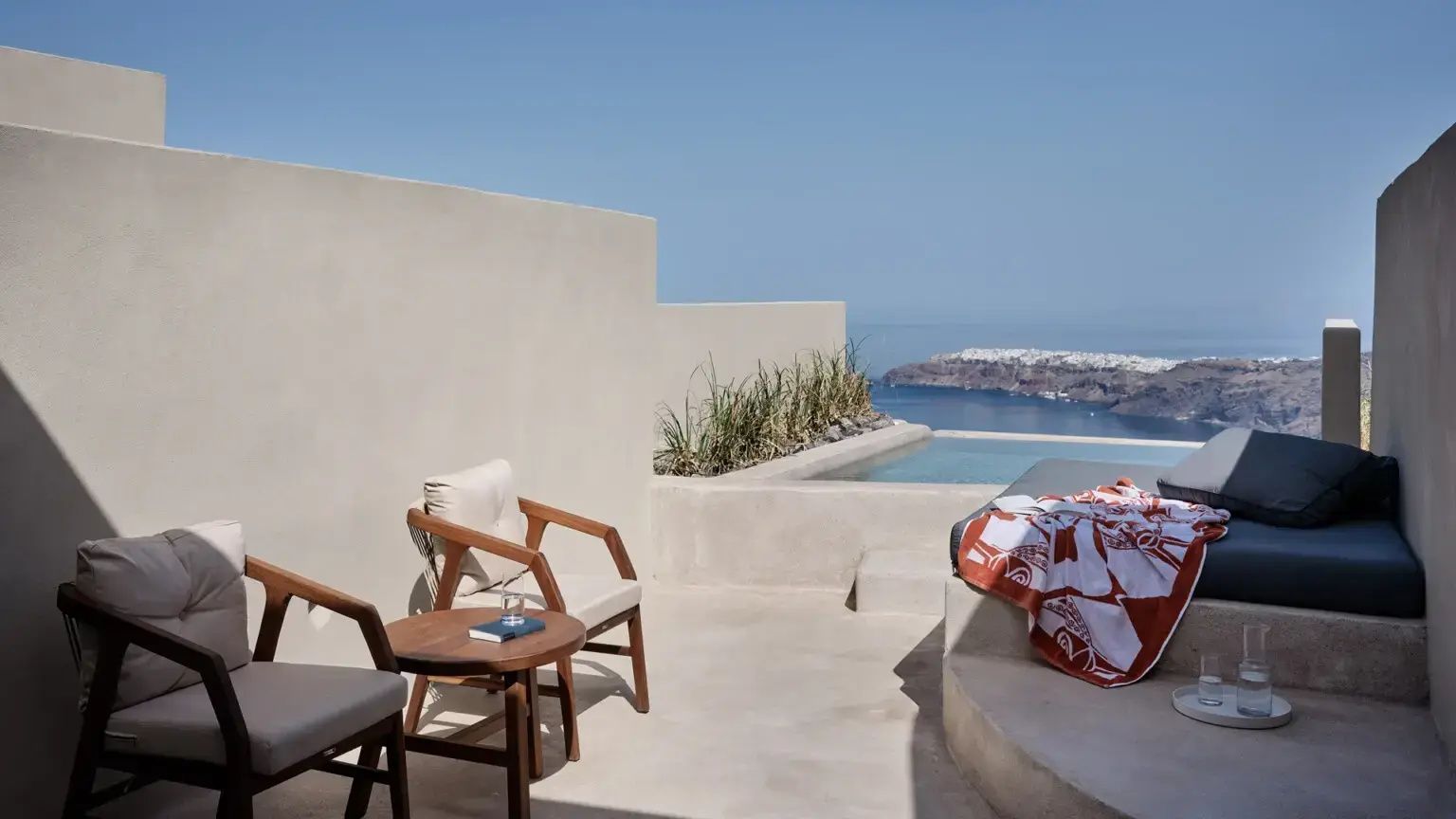 Sonnige Terrasse mit Holzstühlen, kleinem Pool und Blick auf das Meer und die Küste.