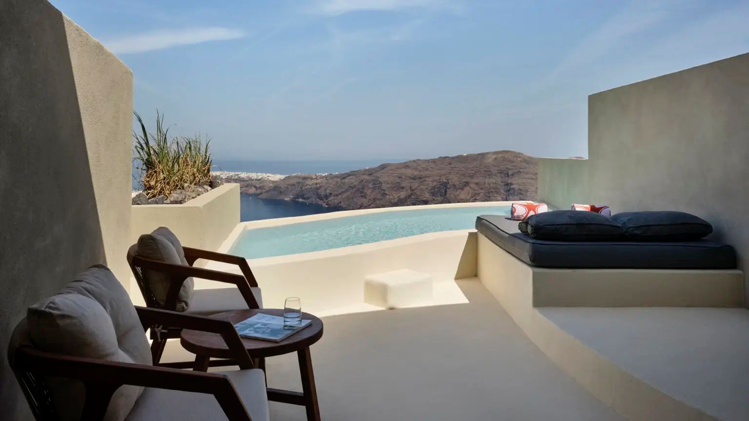 Terrasse mit Holzstühlen, kleinem Pool und Panoramablick auf die Vulkanfelsen und das Meer.