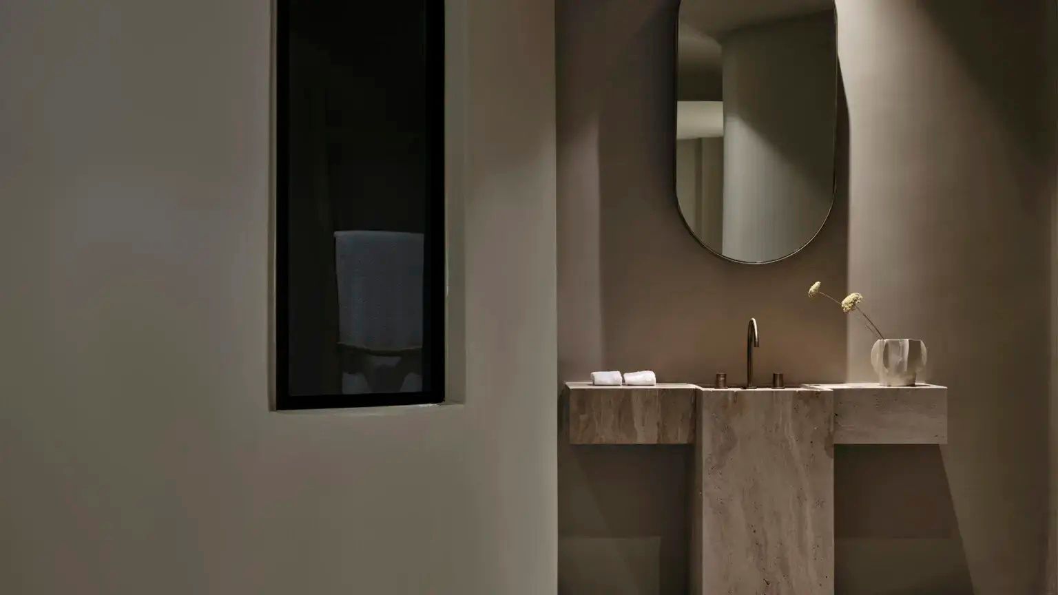 Badezimmer mit Waschtisch aus Naturstein, ovalem Wandspiegel und dezenter Beleuchtung.
