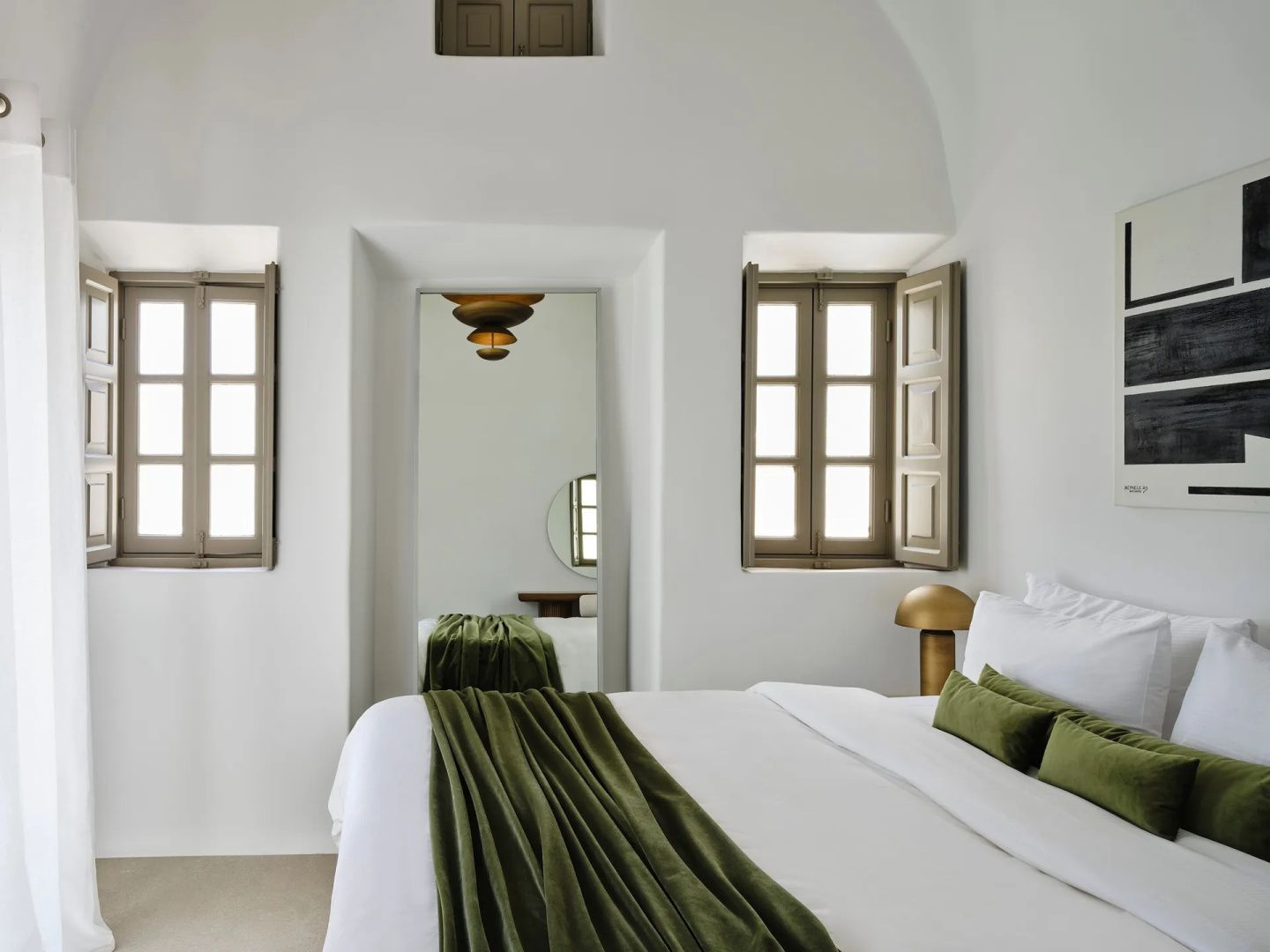 Weißes Schlafzimmer mit Doppelbett, grüner Tagesdecke und Holzfensterläden.