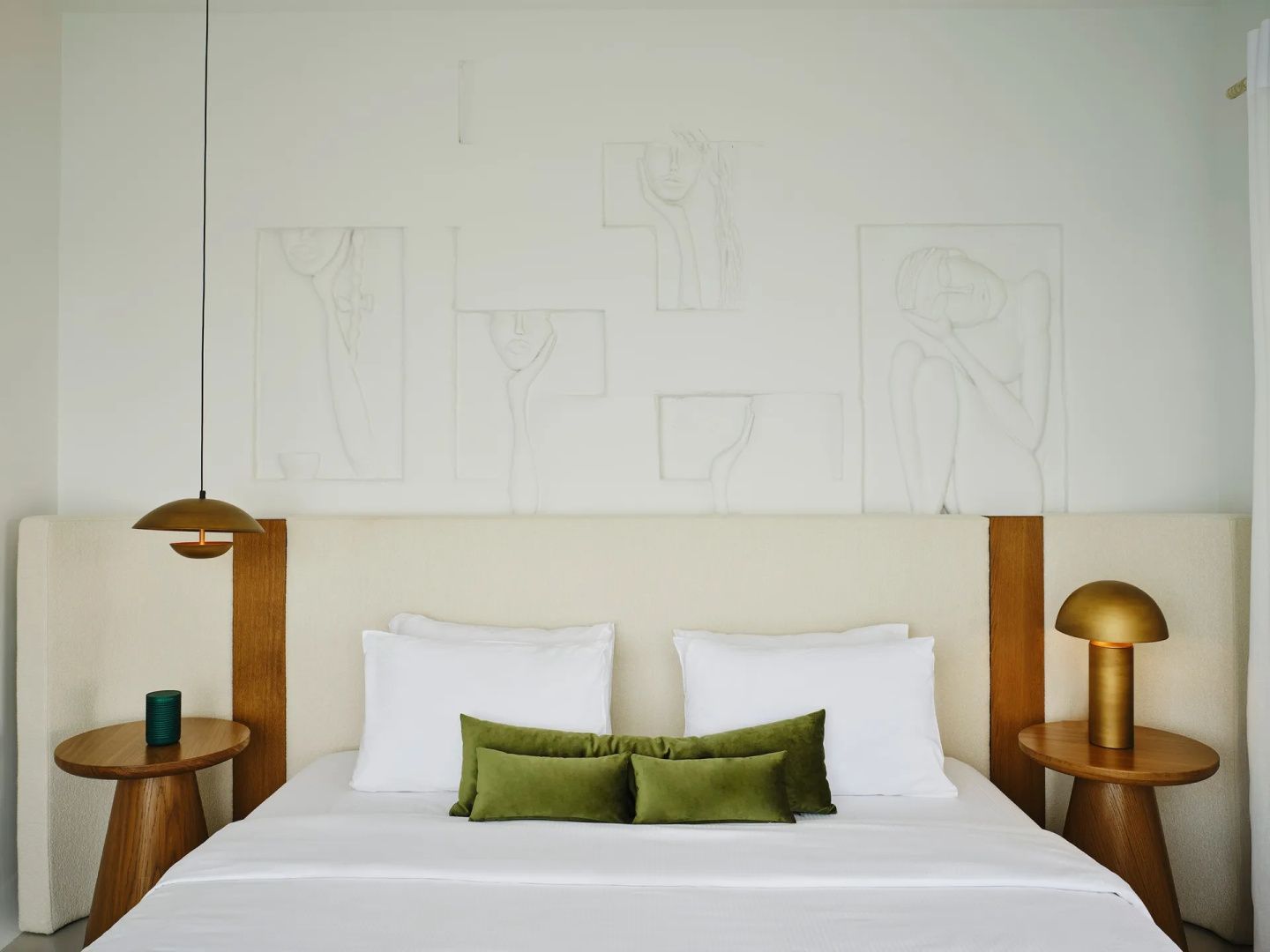 Doppelbett mit weißer Bettwäsche, grünen Zierkissen und minimalistischen Kunstwerken an der Wand.
