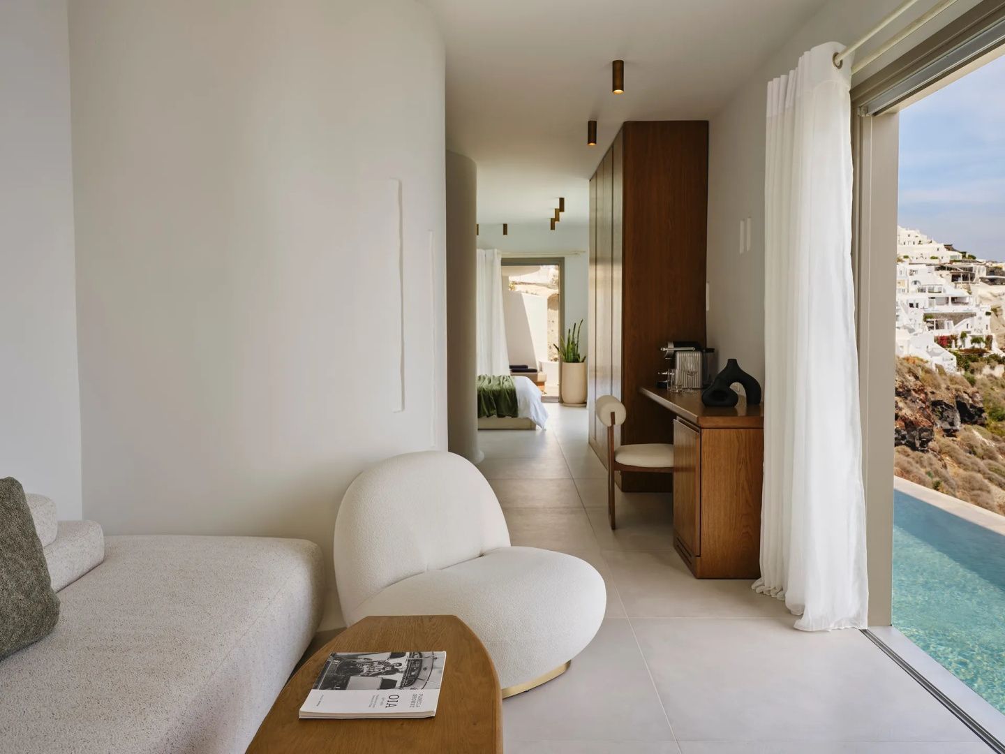 Helles Wohnzimmer einer Suite mit weichem Sessel, Holzschreibtisch und Blick ins Schlafzimmer.