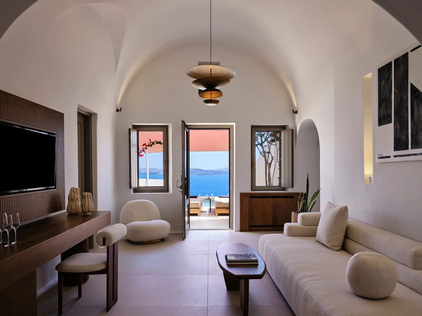 Hell eingerichteter Wohnbereich in Gewölbebauweise mit Sofa, Sessel und Blick aufs Meer.