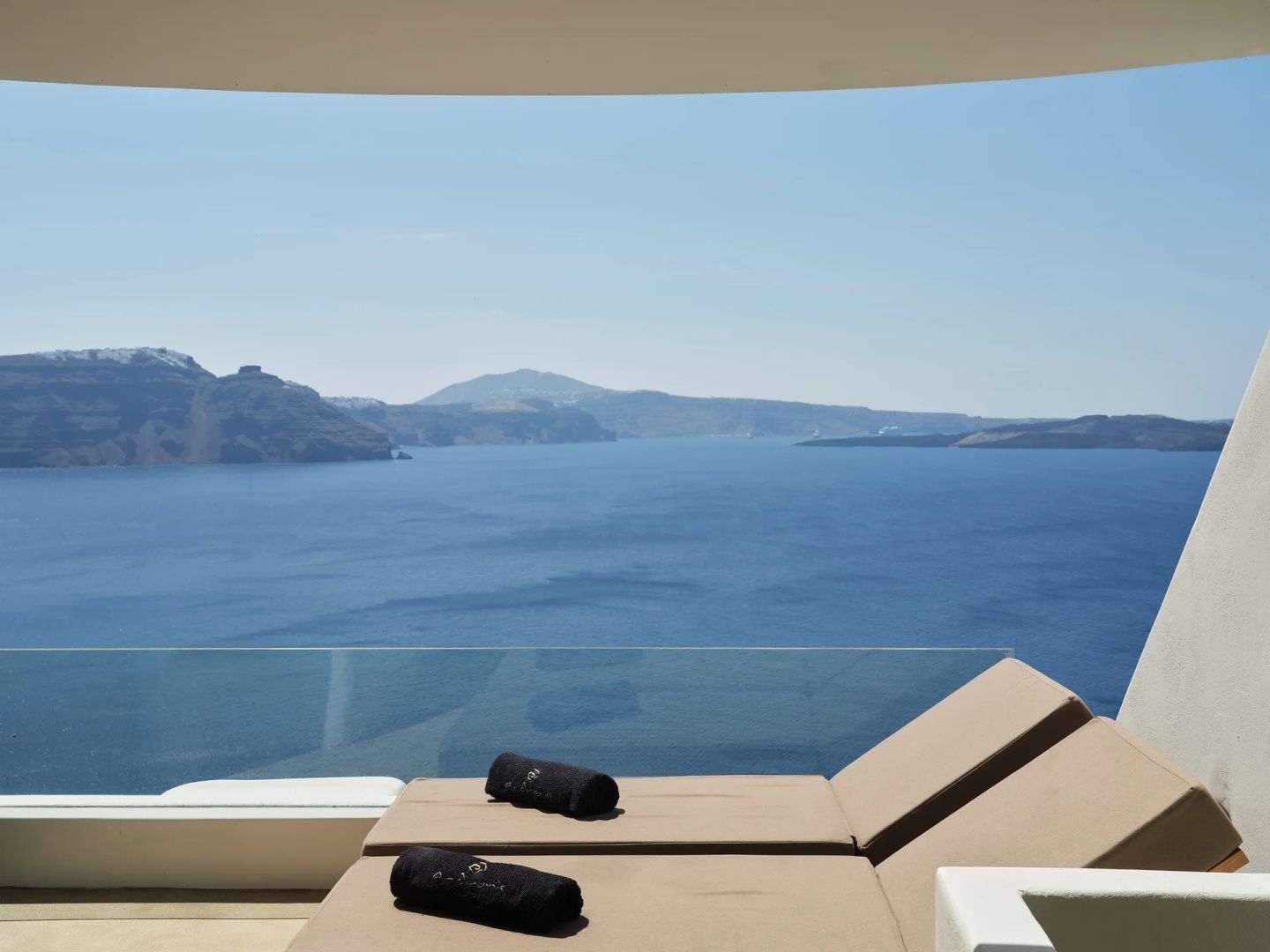 Blick von einer Terrasse mit Liegen auf das blaue Meer und die vulkanische Kraterlandschaft.