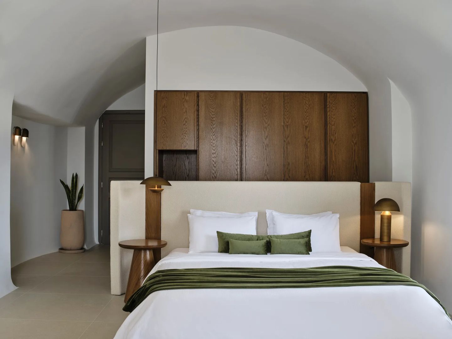 Doppelbett mit grünen Kissen in einem hellen Zimmer mit gewölbter Decke und Holzelementen.