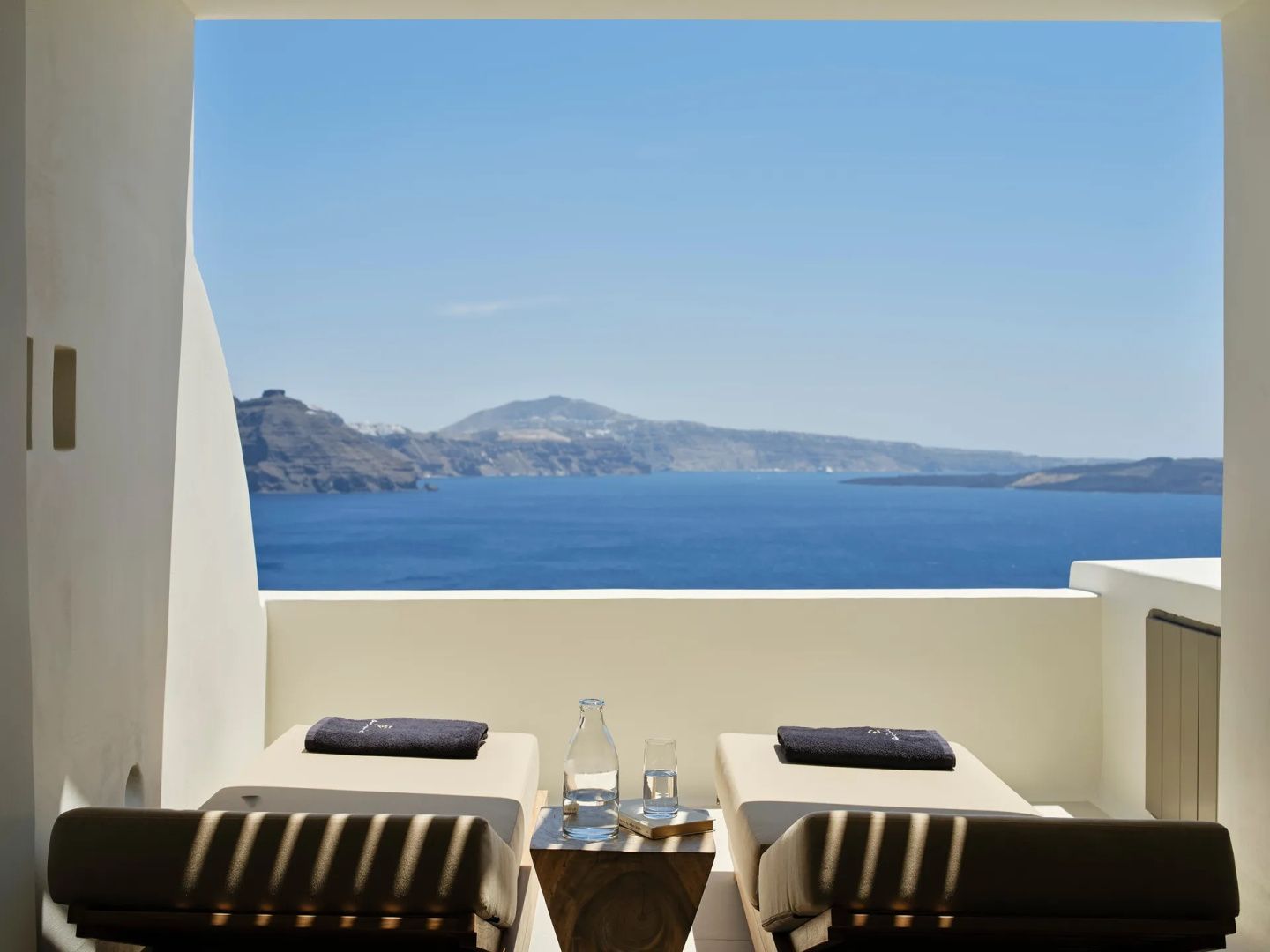 Zwei Sonnenliegen auf einer weißen Terrasse mit direktem Ausblick auf das Meer und Hügel.