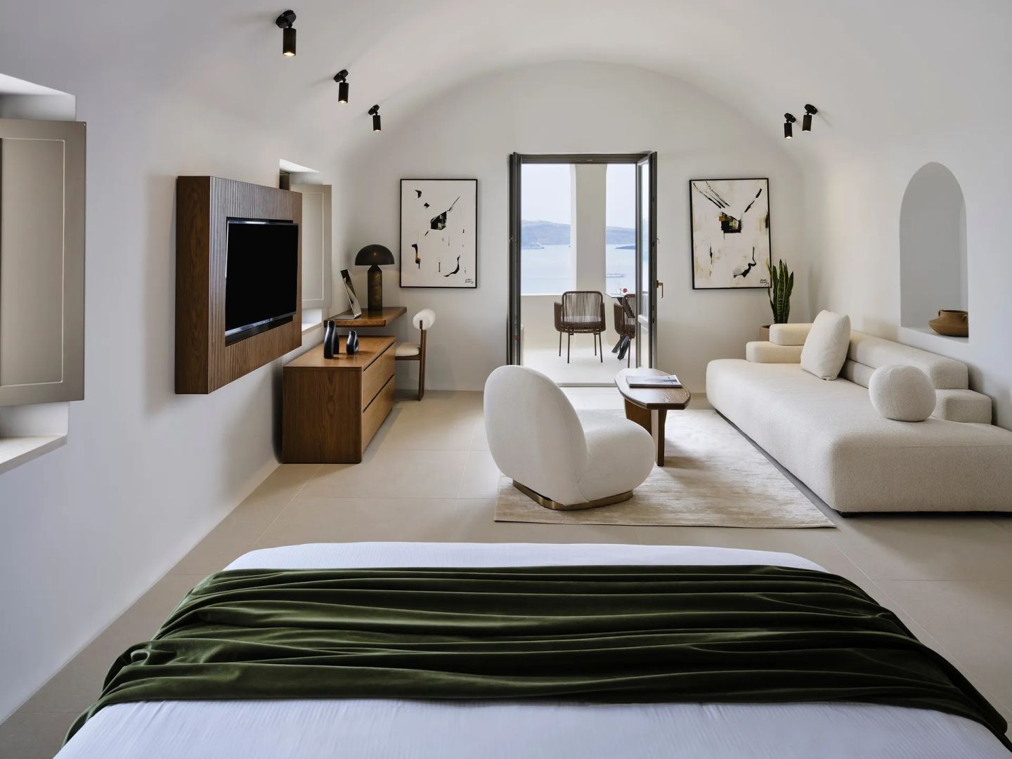 Heller Wohnbereich mit Sofa, Sesseln, Fernseher und freiem Durchgang zur Außenterrasse.