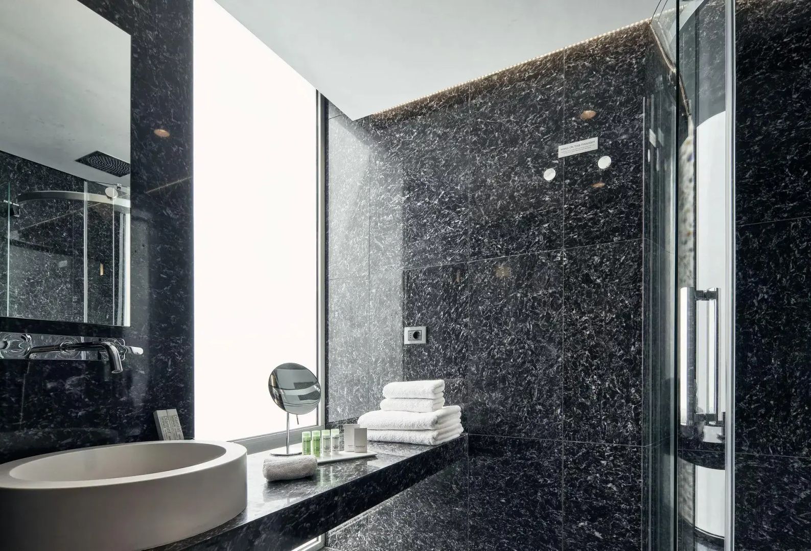 Badezimmer mit dunkler Marmorwand, Waschtisch, Kosmetikspiegel und Handtüchern
