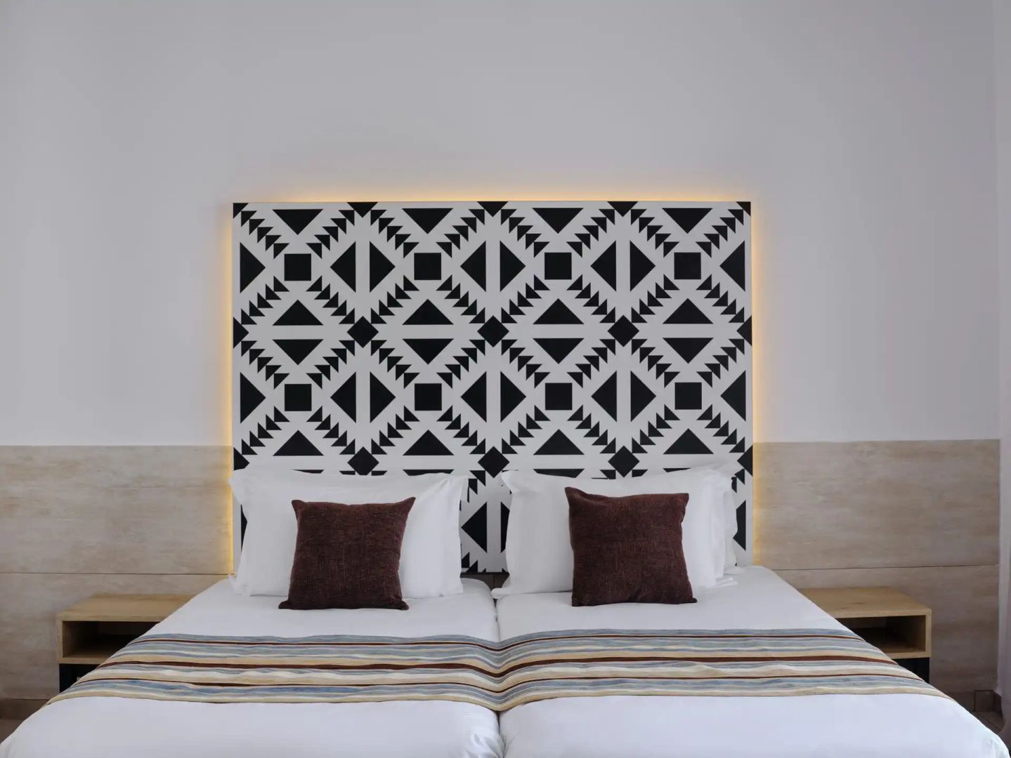 Doppelbett mit weißer Bettwäsche, braunen Kissen und einem schwarz-weiß gemusterten Kopfteil.