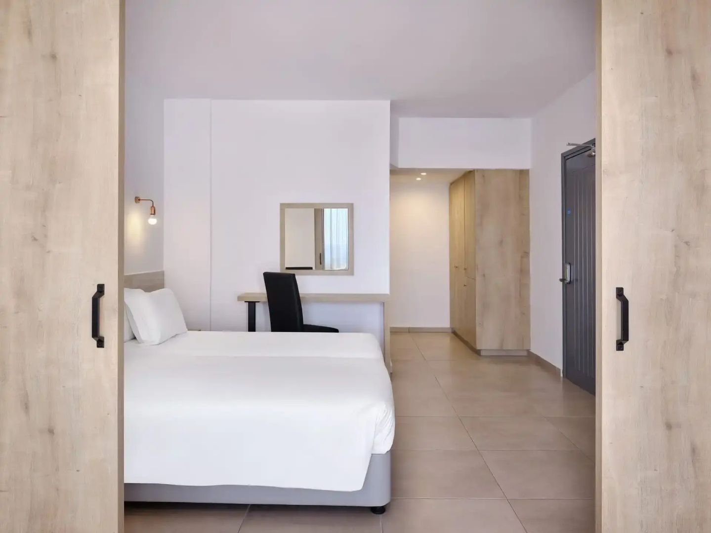 Helles Hotelzimmer mit weißem Doppelbett, Holzmöbeln und Schreibtisch.
