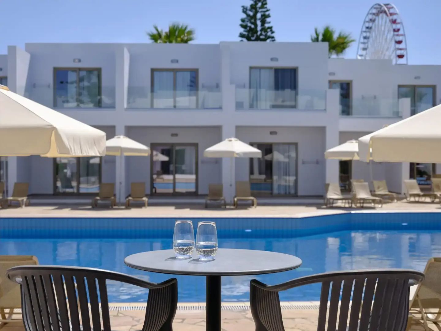 Sitzbereich auf der Terrasse mit Blick über den Swimmingpool und die weißen Hotelgebäude.