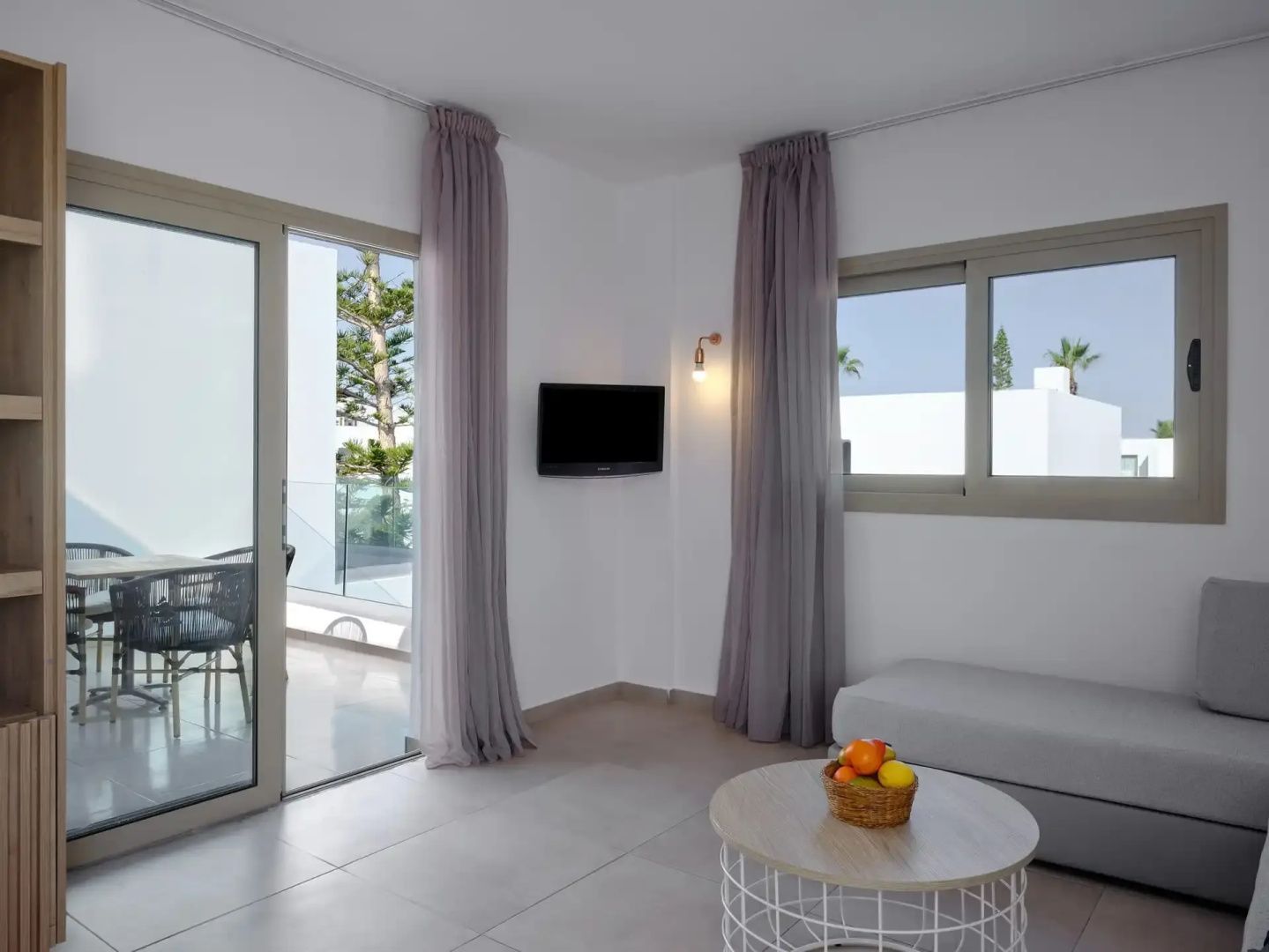 Helles Wohnzimmer mit Sofa, Couchtisch, TV an der Wand und Zugang zum Balkon.