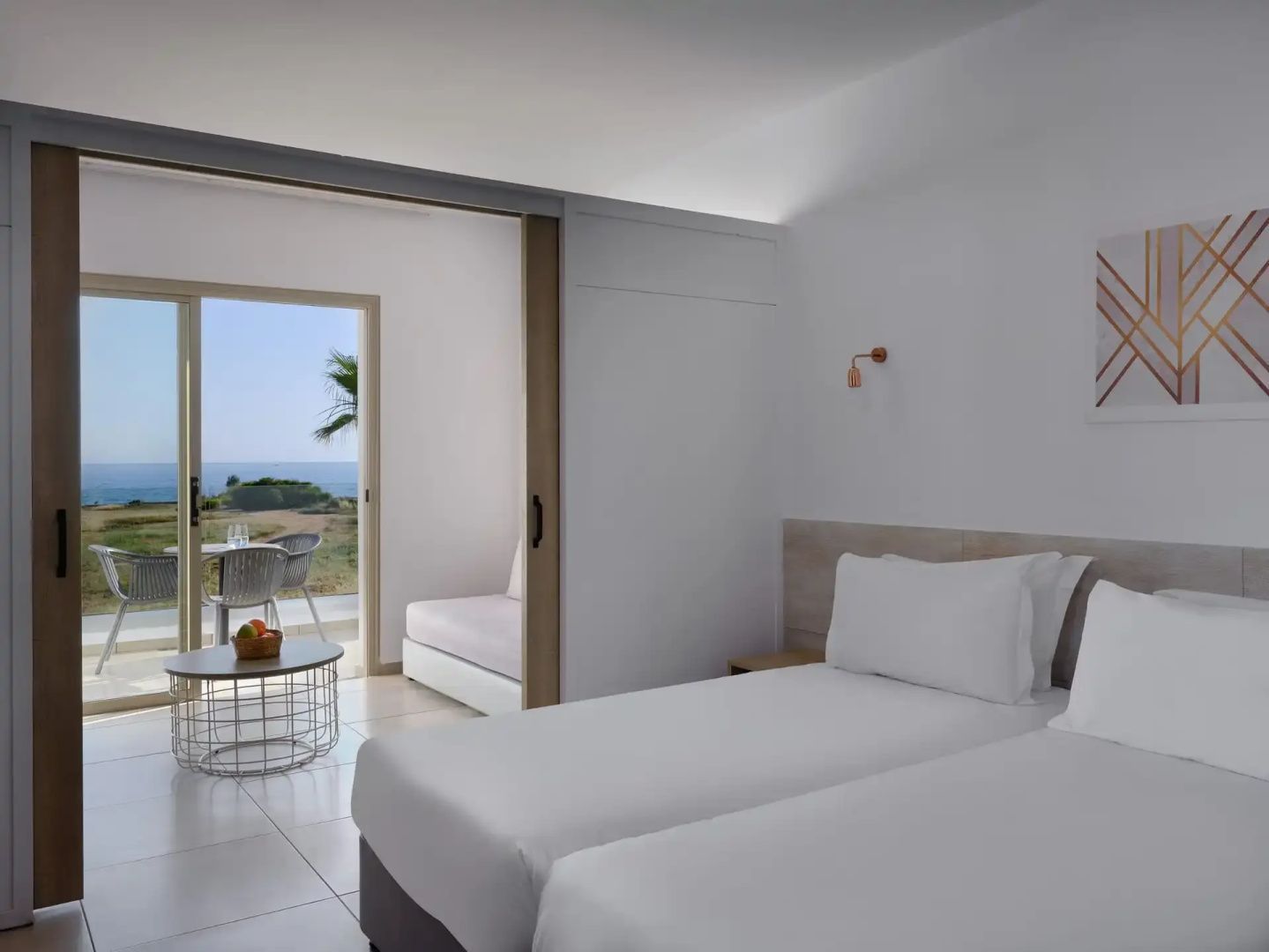 Hell eingerichtetes Hotelzimmer mit zwei Einzelbetten und Durchgang zum Balkon mit Meerblick.