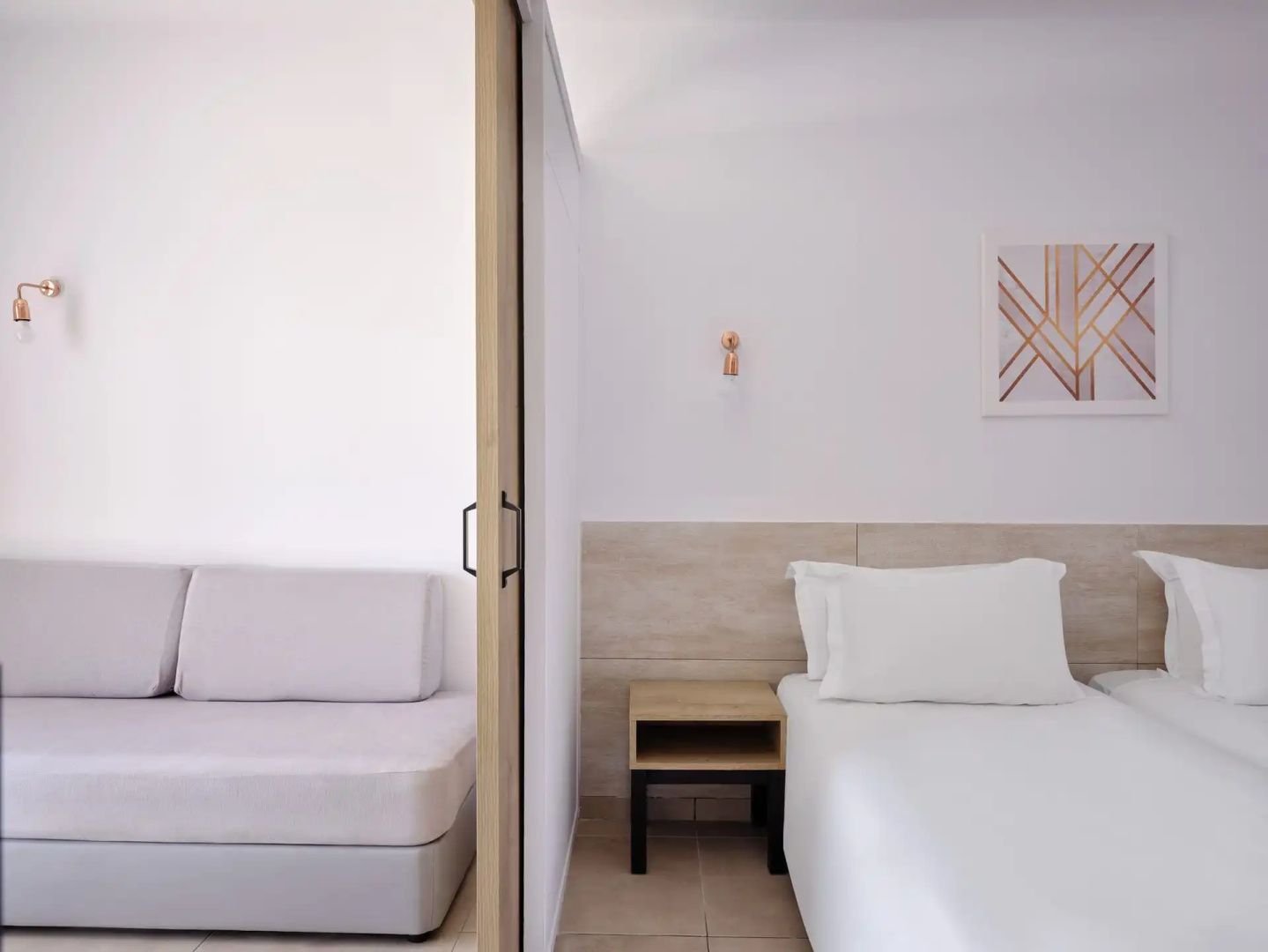 Modern eingerichteter Schlafbereich mit weißem Bett und angrenzendem Sitzbereich.