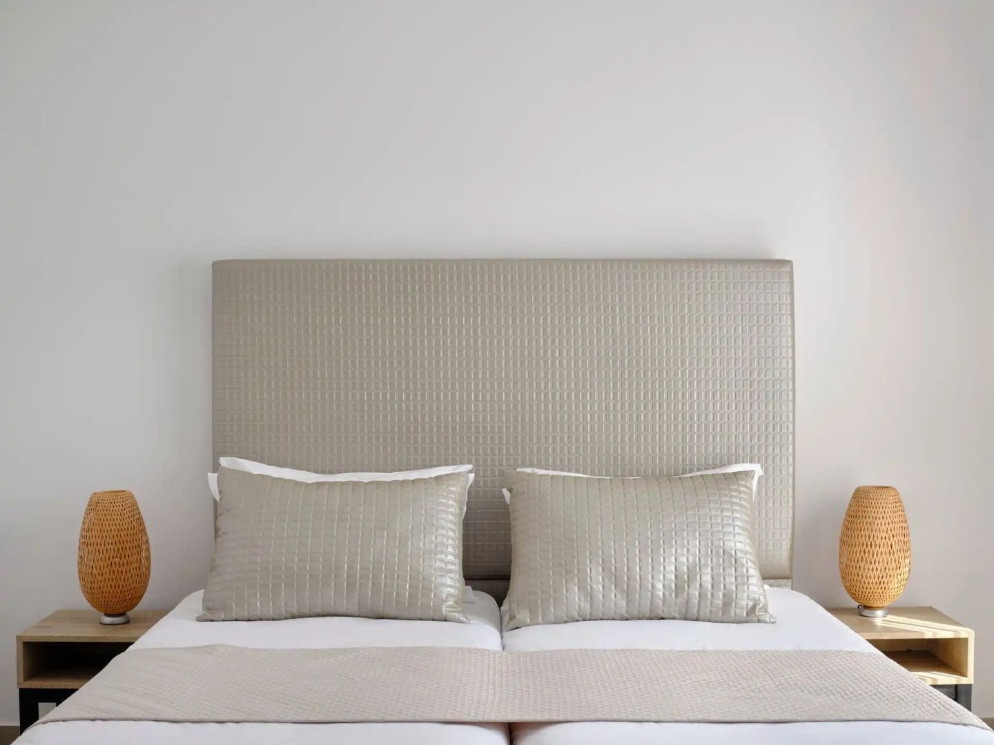 Doppelbett mit beige gepolstertem Kopfteil und zwei passenden Dekokissen.